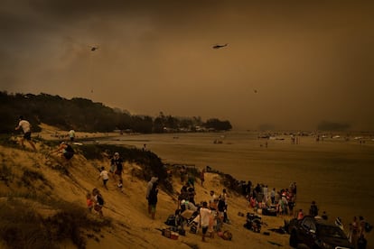 Turistas buscan refugio del fuego a orillas del lago Conjola, en la costa sur de Nueva Gales del Sur, mientras los helicópteros recargan agua para luchar contra las llamas.