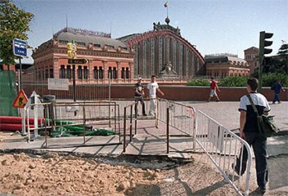 Algunos viandantes atraviesan la acera de la glorieta de Atocha afectada por las obras.