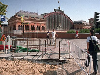 Algunos viandantes atraviesan la acera de la glorieta de Atocha afectada por las obras.