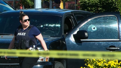 A police officer walks next to a car with bullet holes on the windows at a crime scene in Langley, Canada.