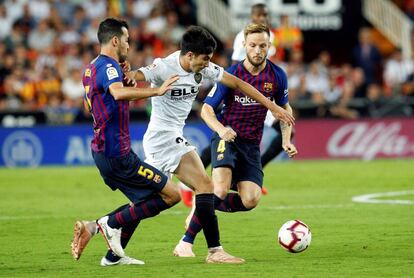 Busquets y Rakitic disputan el balón con Carlos Soler. 