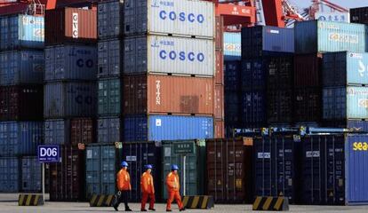 Tres trabajadores frente a varios contenedores de transporte en el puerto de Qingdao, este de China.