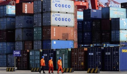 Três trabalhadores diante de vários contêineres no porto de Qingdao, leste da China.