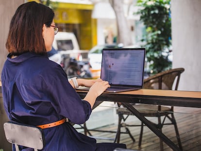 Una mujer usa un portátil al aire libre en un café.