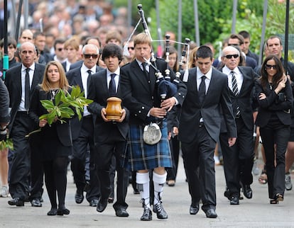 Javier Ballesteros porta la cenizas de su padre, flanqueado a su derecha por su hermana Carmen. El cortejo va precedido por una gaita escocesa en las calles de Pedreña.