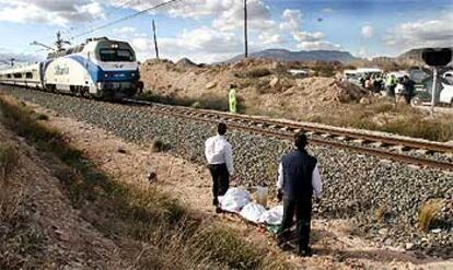 Empleados de la funeraria retiraban ayer uno de los cadáveres mientras un tren circulaba por el lugar del accidente.