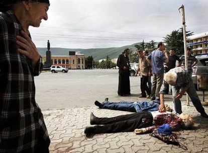 Un grupo de personas observa los cuerpos de dos civiles víctimas de los bombardeos en Gori, la ciudad natal de Stalin, cuya estatua se ve al fondo.