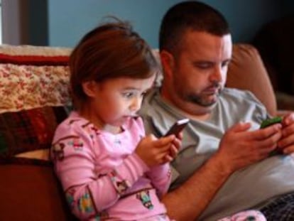 Uma menina e seu pai concentrados nos celulares.