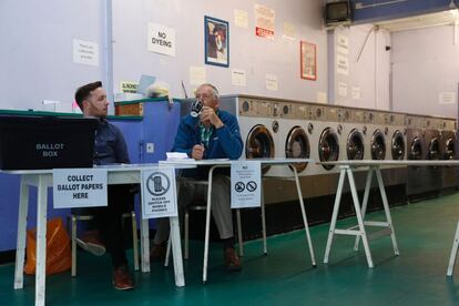 Los miembros de una mesa electoral esperan la llegada de votantes en una lavandería utilizada como centro de votaciones en Headington, a las afueras de Oxford (Reino Unido). 