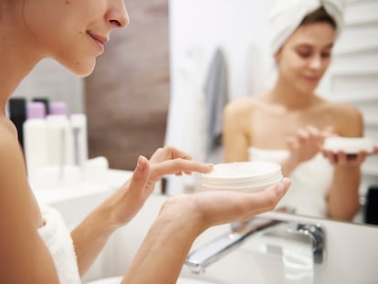Una mujer aplicándose crema hidratante en el baño.