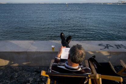 Un hombre lee en la Ribeira das Naus, al lado del río Tajo.