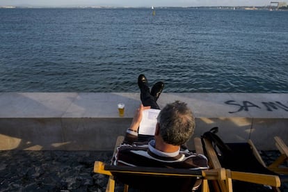 Un hombre lee en la Ribeira das Naus, al lado del río Tajo.