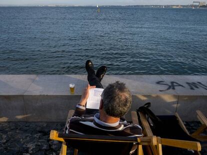 Un hombre lee en la Ribeira das Naus, al lado del río Tajo.