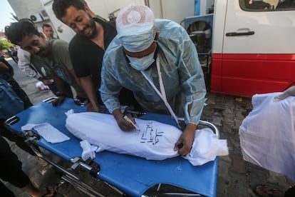 Un trabajador sanitario escribía sobre el cadáver de un menor tras un bombardeo israelí, este martes en el hospital de los Mártires de Al Aqsa en Deir al Balah, en el sur de la franja de Gaza.