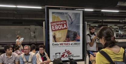 Unos turistas esperan un tren en la estación de Barcelona Sants junto a un cartel de lucha contra el ébola en 2014.