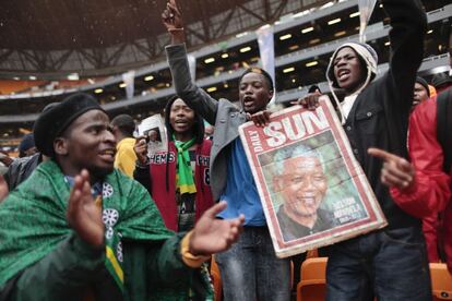 Miles de sudafricanos cantan y bailan protegidos de la lluvia por los paraguas en el estadio FNB de Soweto, Johannesburgo, donde hoy va a celebrarse el servicio religioso oficial por el expresidente.