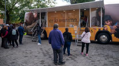 Varias personas esperan para entrar en un autobús que informa sobre el ingreso mínimo vital, en 2022 en Parla (Madrid).