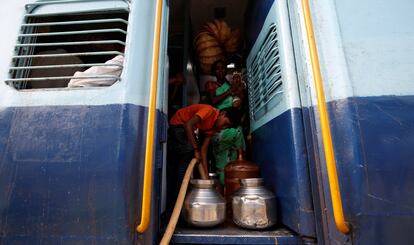 Una madre sostiene a su hija de cuatro meses mientras observa a su vecino, un niño de 13 años, llenando los recipientes con agua en la estación de tren de Aurangabad (India).