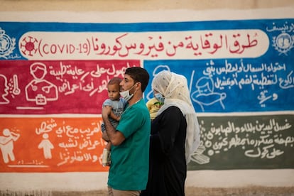 Una familia pasa frente a un mural de UNICEF y la Organización Mundial de la Salud, que contiene instrucciones para evitar los contagios por covid, en la ciudad siria de mayoría kurda de Qamishli, donde ha tenido lugar un pico de contagios en los últimos días.