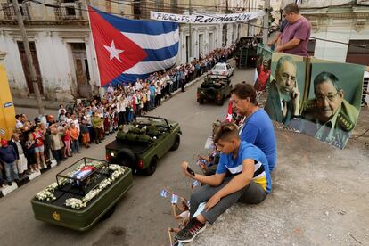 Una familia se sienta a un lado de una fotografía de los hermanos Castro, mientras los restos de Fidel son transportados de La Habana a Santiago de Cuba, el 1 de diciembre de 2016.