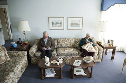 Una pareja de ancianos en el salón de su casa, sentados en el sofá.