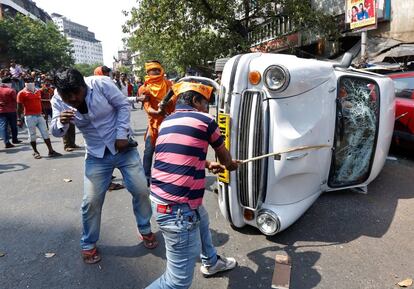 Un partidario del Partido Popular Indio golpea un coche volcado durante una protesta en Calcuta, India.