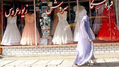 Una joven afgana pasa frente a un escaparate de vestidos de novia de colores blanco, rosa y rojo que se alquilan en Kabul.