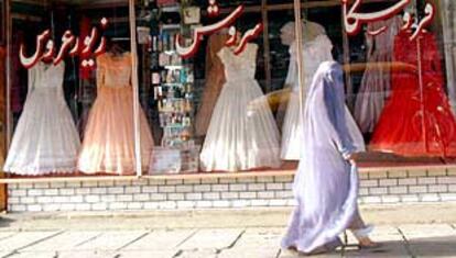 Una joven afgana pasa frente a un escaparate de vestidos de novia de colores blanco, rosa y rojo que se alquilan en Kabul.