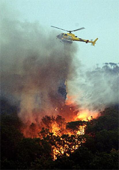 Un helicóptero lanza agua sobre las llamas en la urbanización Altaba de Maçanet.