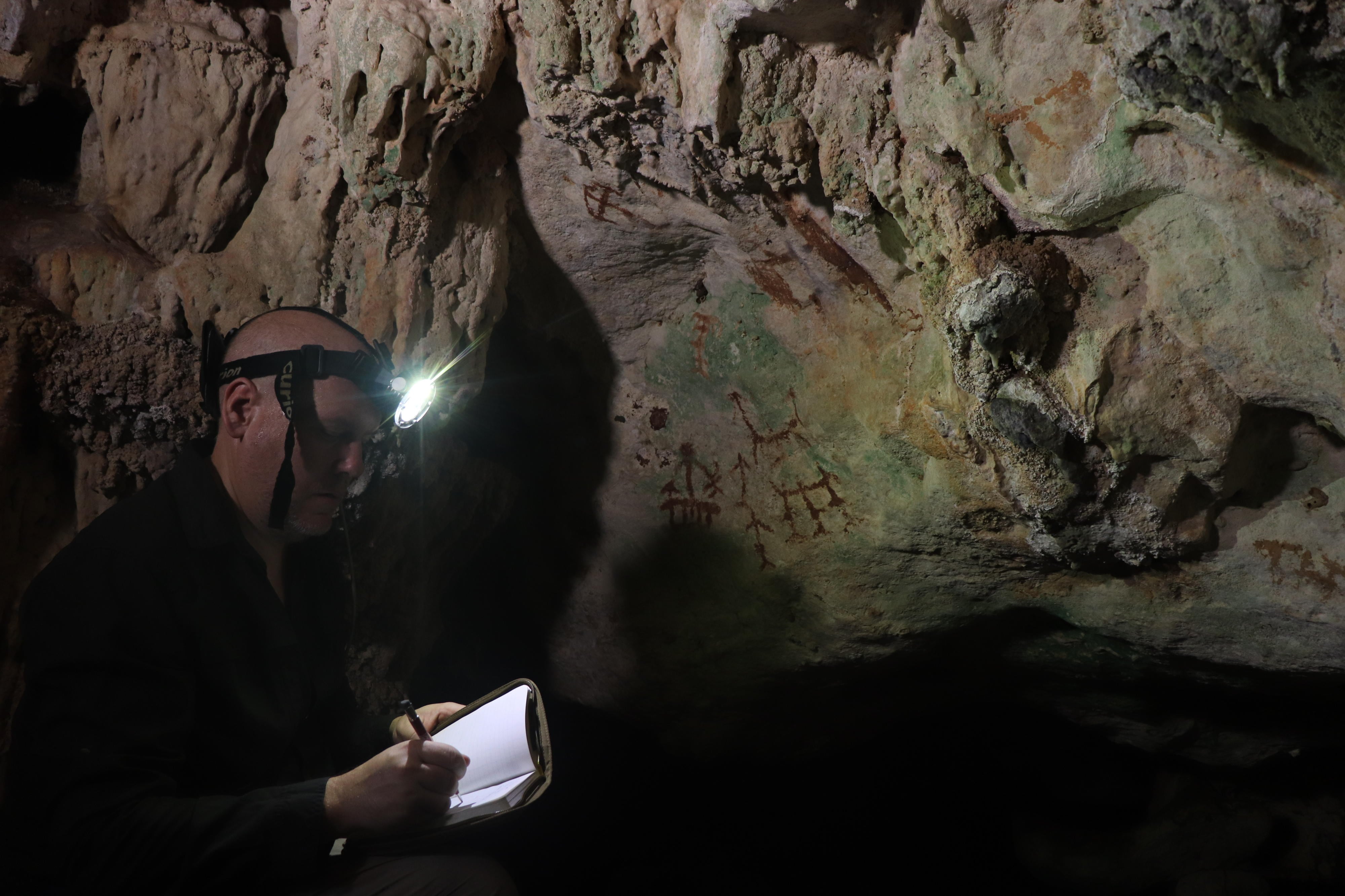 El arqueólogo Maxime Aubert examina unas pinturas rupestres en la cueva de la isla de Muna, en Indonesia.
