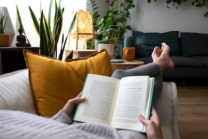 Una mujer se relaja leyendo un libro en el sofá.