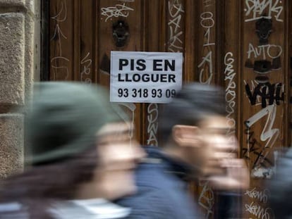 Tres jóvenes pasan ante el cartel de un piso en alquiler, en Barcelona.