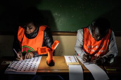 Los colegios electorales recurren en Zambia a unas elementales lamparillas portátiles para poder contar los votos. En la imagen, miembros de la Comisión Electoral de Zambia comprueban el registro de electores y los votos emitidos.