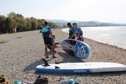 Brittany Pummell (en cuclillas) prepara el equipo para la clase de SUP en la playa de Skala Oropou, al norte de Atenas, mientras los tres chicos, todos refugiados afganos, escuchan atentamente sus instrucciones.