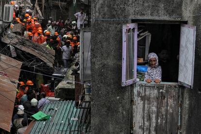 Una mujer mira por la ventana de su casa mientras trabajadores de rescate buscan supervivientes en un edificio contiguo que se derrumbó en Bombay (India), el 16 de julio de 2019.