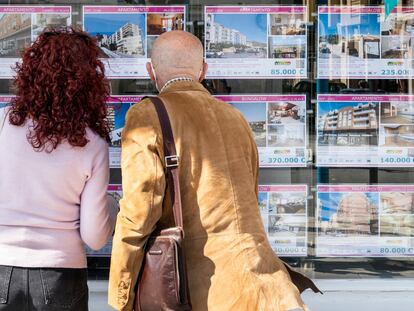 Dos clientes miran los carteles de venta y alquiler de casas en una agencia inmobiliaria de Alicante.