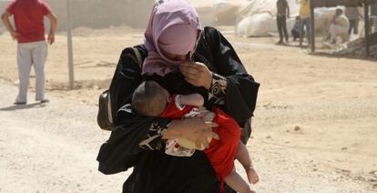 Una refugiada siria lleva a su hijo en brazos mientras camina entre una tormenta de arena en Mafraq (Jordania).