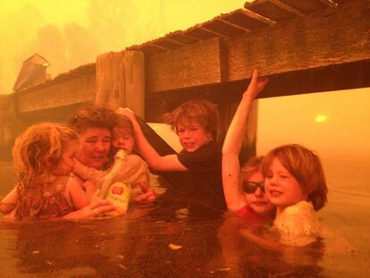 La familia Holmes se protege bajo un embarcadero del avance del fuego que destruyó 90 casas en Tasmania, Australia el 4 de enero.