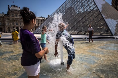 Un grupo de turistas se refresca en las fuentes de la Pirámide del Museo del Louvre en París.
