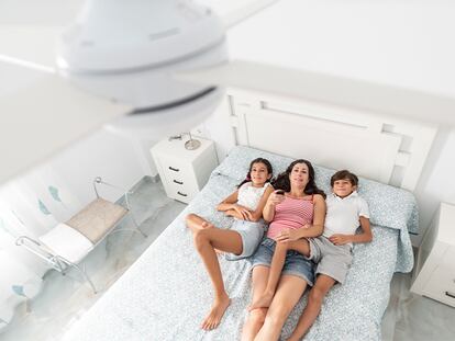 Una madre con sus hijos en la cama encendiendo el ventilador de techo.