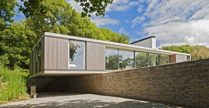 La vivienda, de una sola planta, está ubicada en medio de un terreno inclinado. Para hacer frente a esos cambios de nivel, la casa se desliza sobre un muro de contención y crea un espacio de estacionamiento bajo techo (el que se observa en el lado izquierdo de la fotografía).