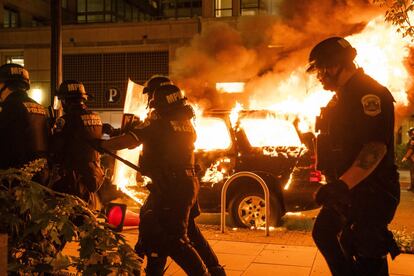 Varios policías pasan frente a un coche ardiendo durante las protestas en Minneapolis.