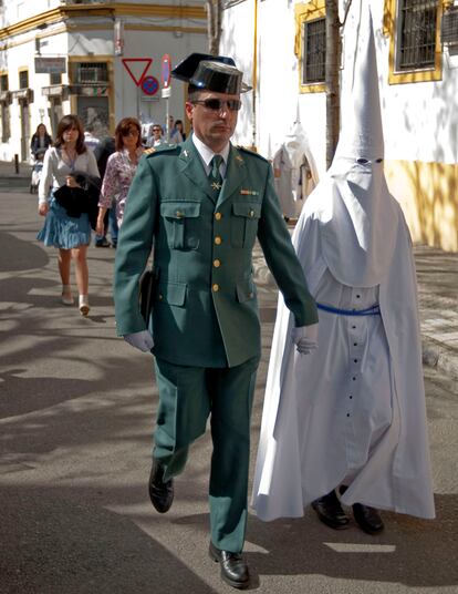 Un guardia civil y un nazareno caminan, cogidos de la mano, hacia la iglesia de San Sebastián, en el barrio sevillano de El Porvenir, desde donde la hermandad de la Virgen de la Paz inicia su estación de penitencia durante el Domingo de Ramos.