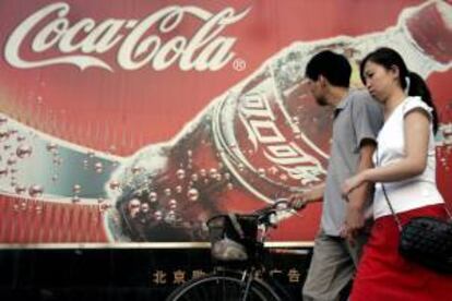 Fotografía de archivo fechada el 14 de junio de 2005 de una pareja pasando delante de un cartel publicitario de Coca-Cola en Pekín, China. EFE/Archivo