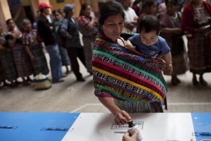Una guatemalteca con su bebé deposita su voto en una urna ayer en San Juan Comalapa.