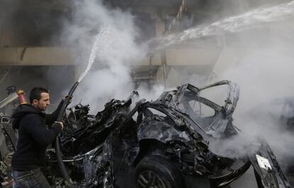 Un hombre intenta apagar uno de los vehículos que ha resultado calcinados tras la explosión de un coche bomba en Beirut (Líbano).