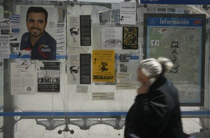 Una mujer habla por el móvil al pasar por una parada de autobús con un cartel del líder de IU Alberto Garzón que concurre en la coalición Unidos Podemos, en una calle de Madrid.