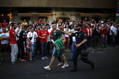 Un aficionado del Real Betis acompa?ado de un polica, pasa junto a aficionados del Sevilla FC.