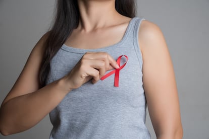 Closeup woman hand holding red ribbon HIV, world AIDS day awareness ribbon. Healthcare and medicine concept.