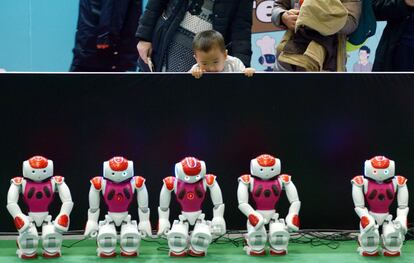 Un niño observa atento a un grupo de robots NAO.